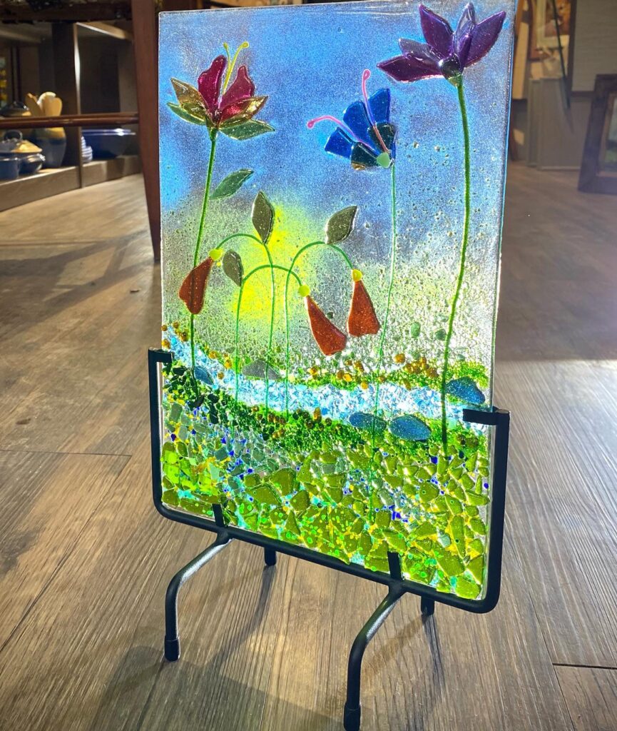 Fused Glass flower scene with blue sky and water elements made with cut and chipped glass by Michelle Manquen.